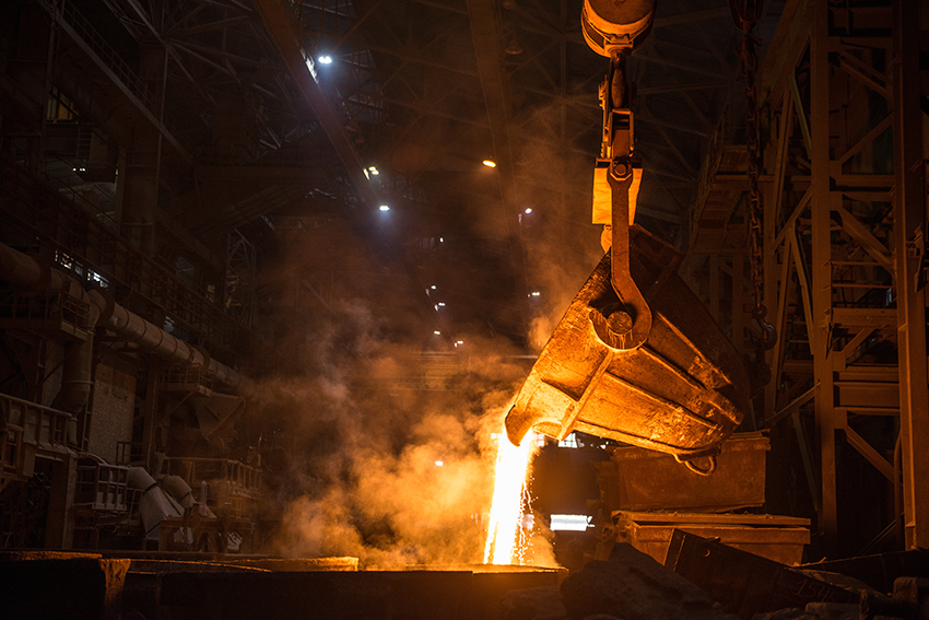 Ladle pouring liquid metal into molds at a steel mill.