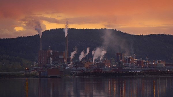 Sunset over the Domsjö plant against a forest backdrop and a river in the foreground.